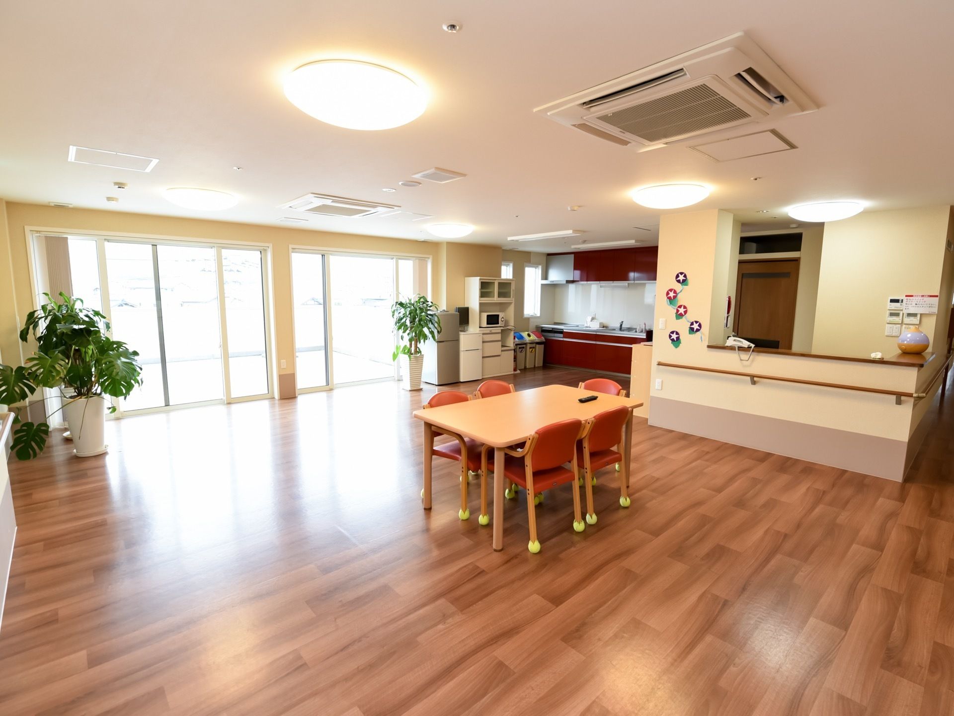 広いリビングには、システムキッチンが備わっている。５脚の椅子がセットされたテーブルや観葉植物が置かれている。