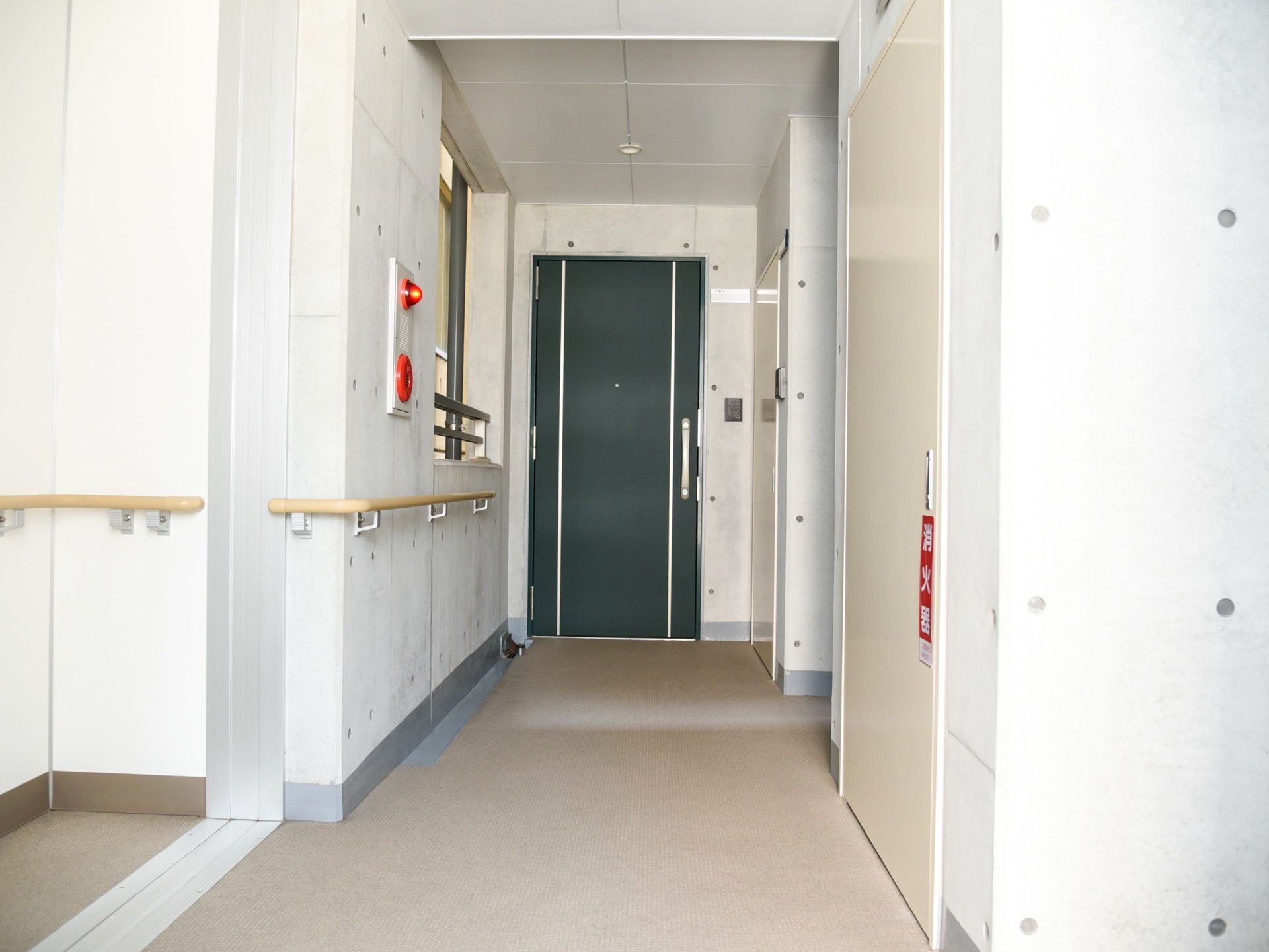通路の壁に手すりが設けられている。火災時の非常ベルと消火器が設置されている。通路の幅は、車椅子で通行可能な広さが確保されている。