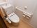 壁に手すりが設けられている。温水洗浄便座のトイレとなっている。大、小の流すボタンが取り付けられている。