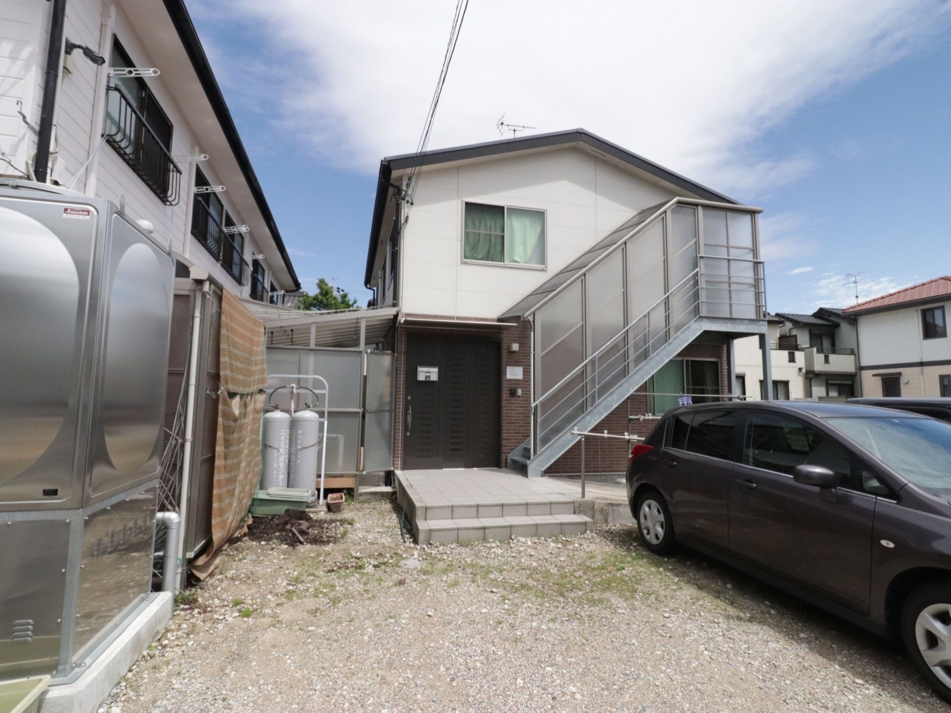 建物の２階から地上に出る外階段が設置してある。駐車場の後ろのスペースには、物干し台と竿を置き、屋外で衣類を干すことができる。