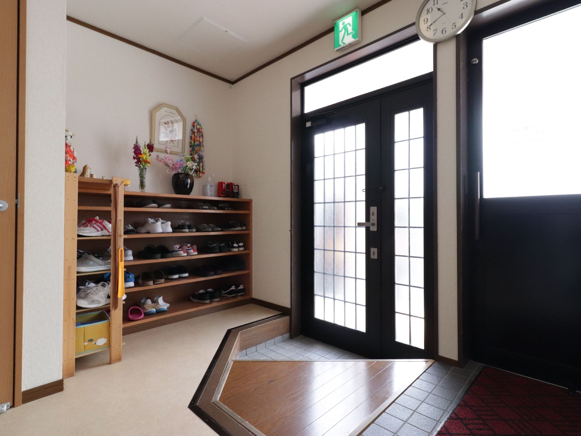 L字に設置された靴箱の棚上に、折り鶴や花を生けた花瓶が飾ってある玄関