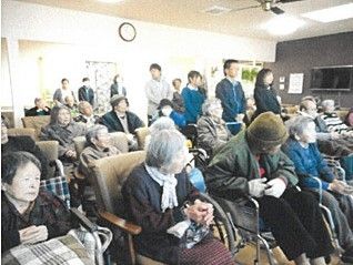 さまざまな目的で使用できる広い部屋である。スタッフや入居者様が集まり、イベントをおこなっている。壁に掛け時計がある。