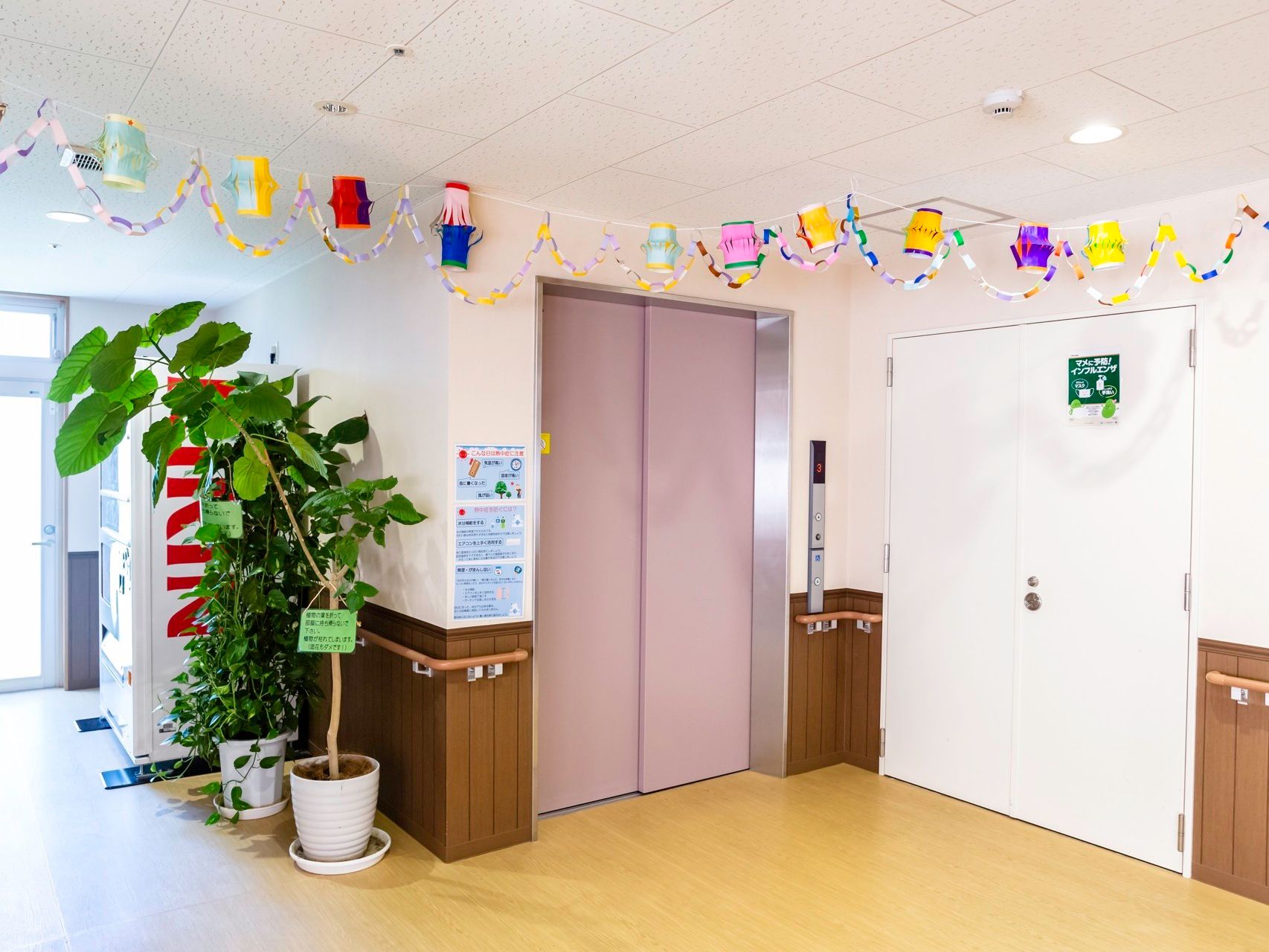 落ち着いたピンク色のエレベーターが設置されている。天井には、入居者様が制作した色とりどりの輪飾りがつるされている。