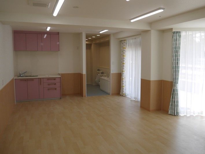 ピンク色のキッチンと吊戸棚を設けた、大きな窓がある広間