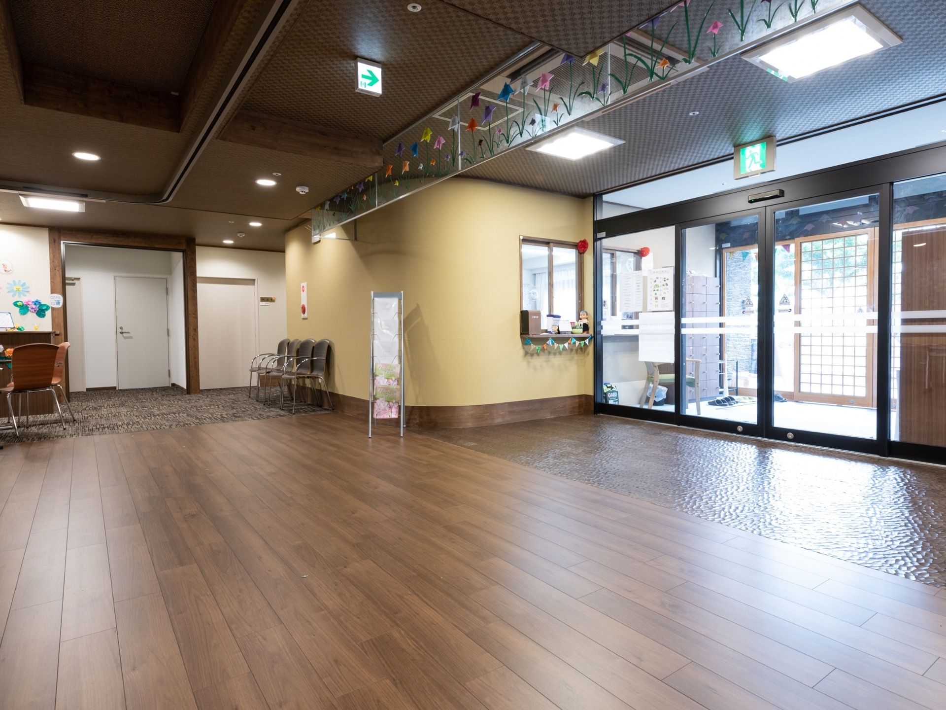 玄関とエントランスの間のドアはガラスの自動扉になっている。スタッフの事務所への受付の窓がある。壁際に椅子が置かれている。
