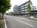 ５階建ての施設は街路樹が並ぶ大通りに面している。建物前に駐車スペースがあり、車や原付バイクが止まっている。