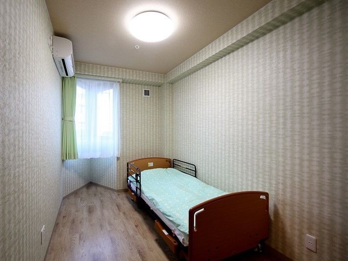 部屋の角に窓を設けた、介護ベッドのある細長い形の居室