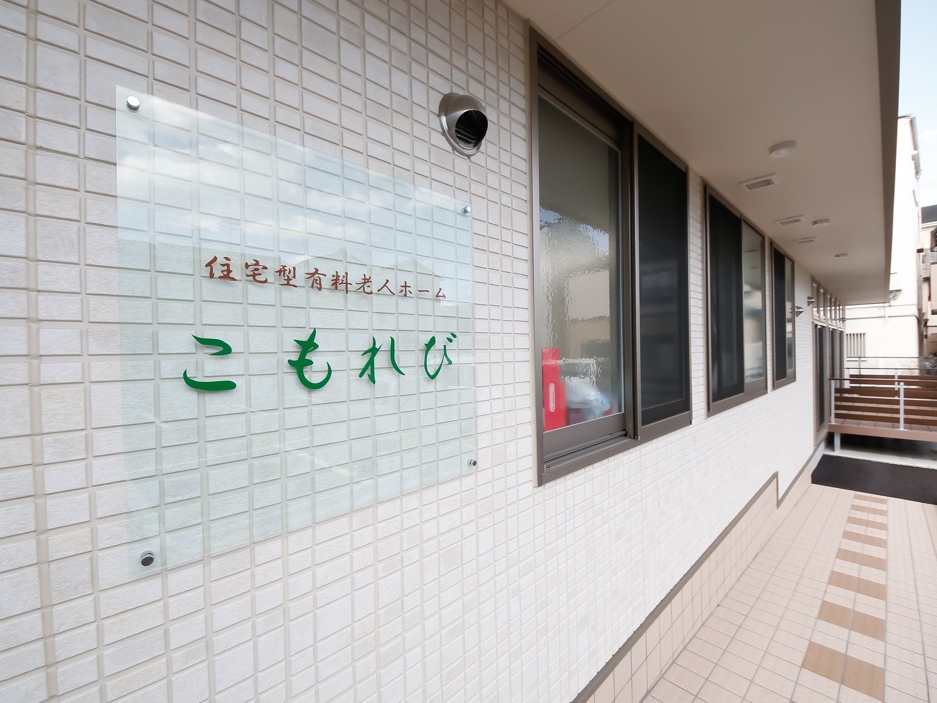 施設の表に施設名である、住宅型有料老人ホームこもれびの看板がかかっている。奥には小さなバルコニーが見える。
