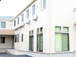 明るい雰囲気の白い外壁の建物である。玄関までの通路には手すり付きのスロープがあり、車椅子をご利用の方も安全に移動することができる。