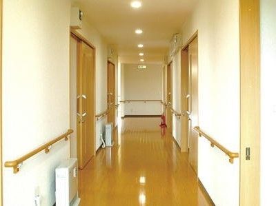 車椅子に座って手を振る高齢女性と後ろで介助をする男性ヘルパー