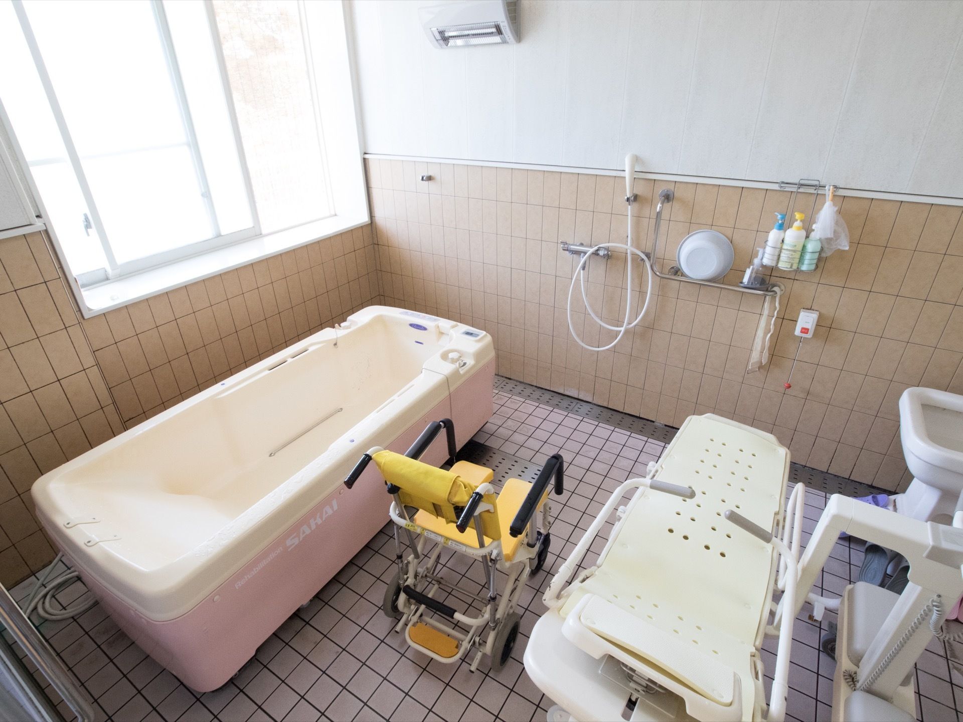大きな窓から明るい日差しの入る浴室。水捌けのよいタイル張りになっており、入浴用のストレッチャーとリフトが設置されている。