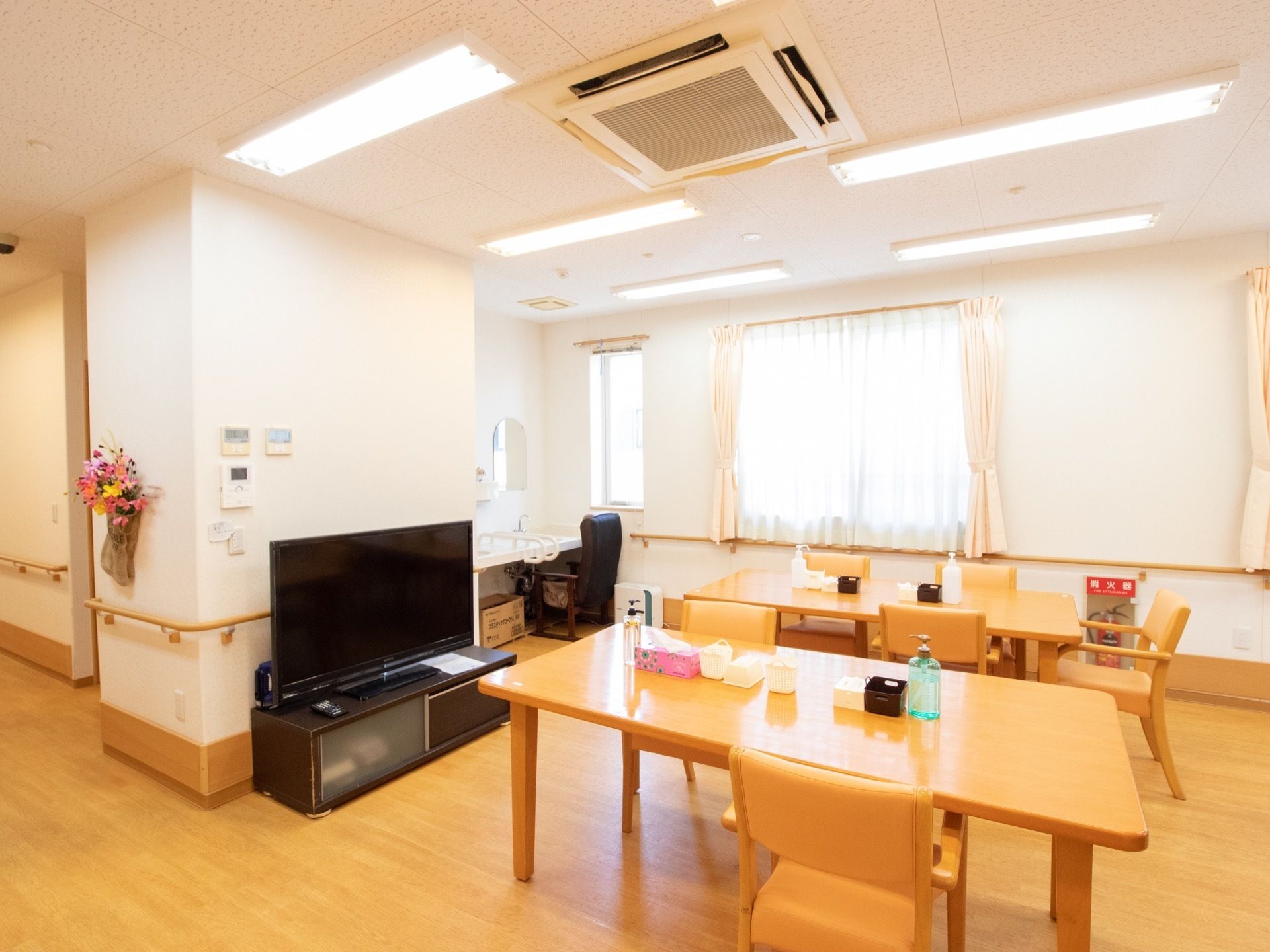テーブルや椅子、テレビが設置された共有スペースである。洗面台があり、その前には黒いソファが置かれている。