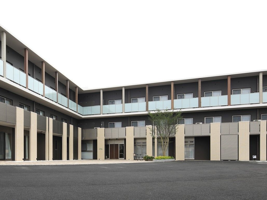 L字型の3階建ての建物の周囲に広がるアスファルトで舗装されて駐車場