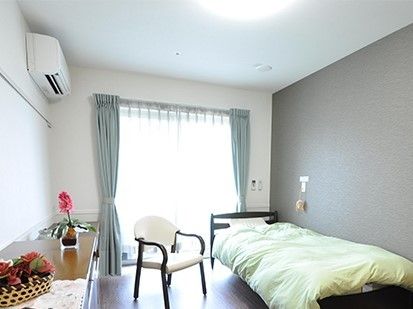 赤い花が活けてある花瓶が置かれたチェストとベッドがある居室