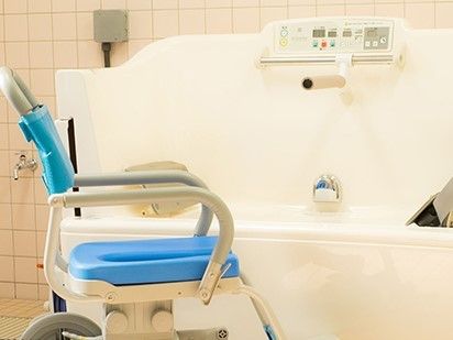 青い浴室用車いすや機械入浴機器が用意されたタイル張りの浴室