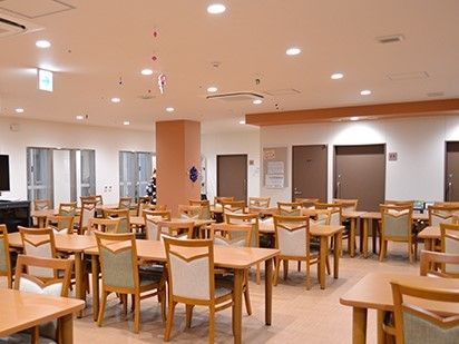 ダイニングテーブルのセットが多数並べられた開放的な空間である。奥にはブラウンを基調とした扉が並んでいる。