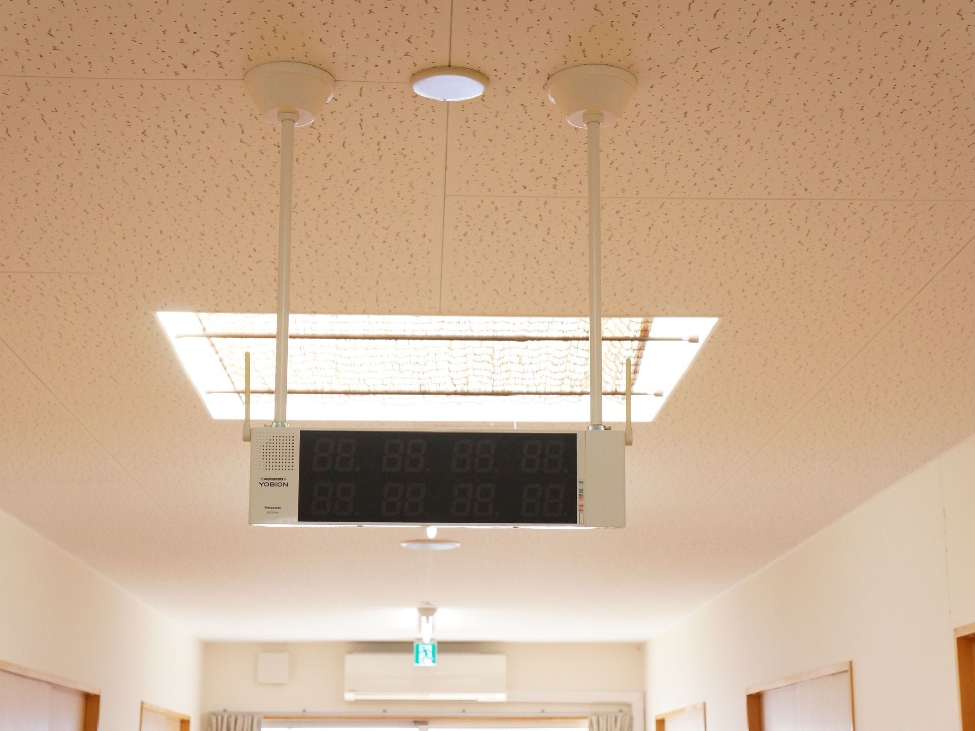大型のLED表示器が天井から吊り下げられている。奥には窓があり、その上に避難誘導灯が設置されている。