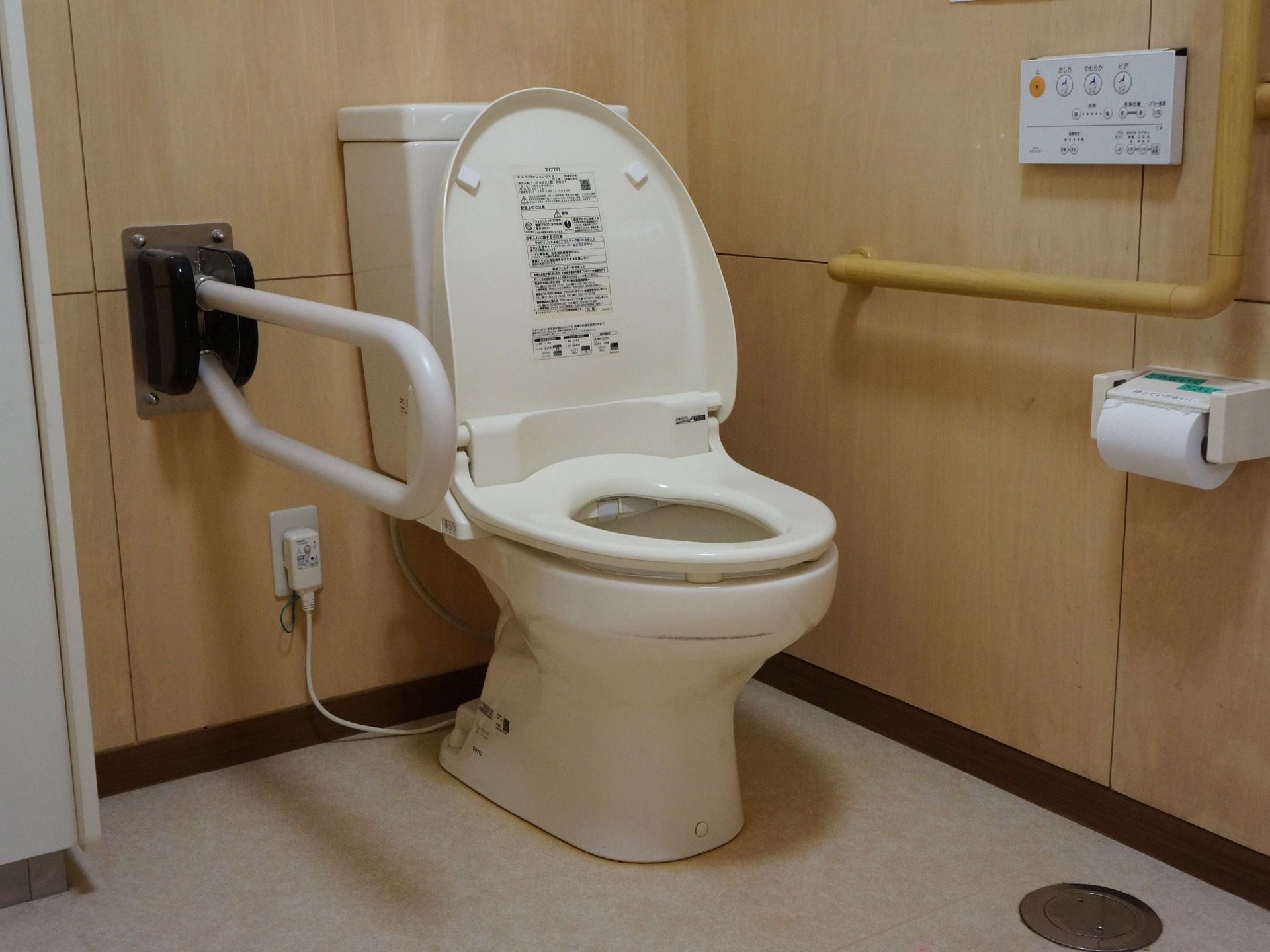 木製パネルの壁のあるトイレで、壁に手すりが設置されている。便器の脇にも可動式の手すりが備わっている。