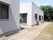 白いレンガ調の外壁の平屋建ての建物が２棟ある。窓に屋根が設置してあり、屋外には歩道と庭が整備されている。