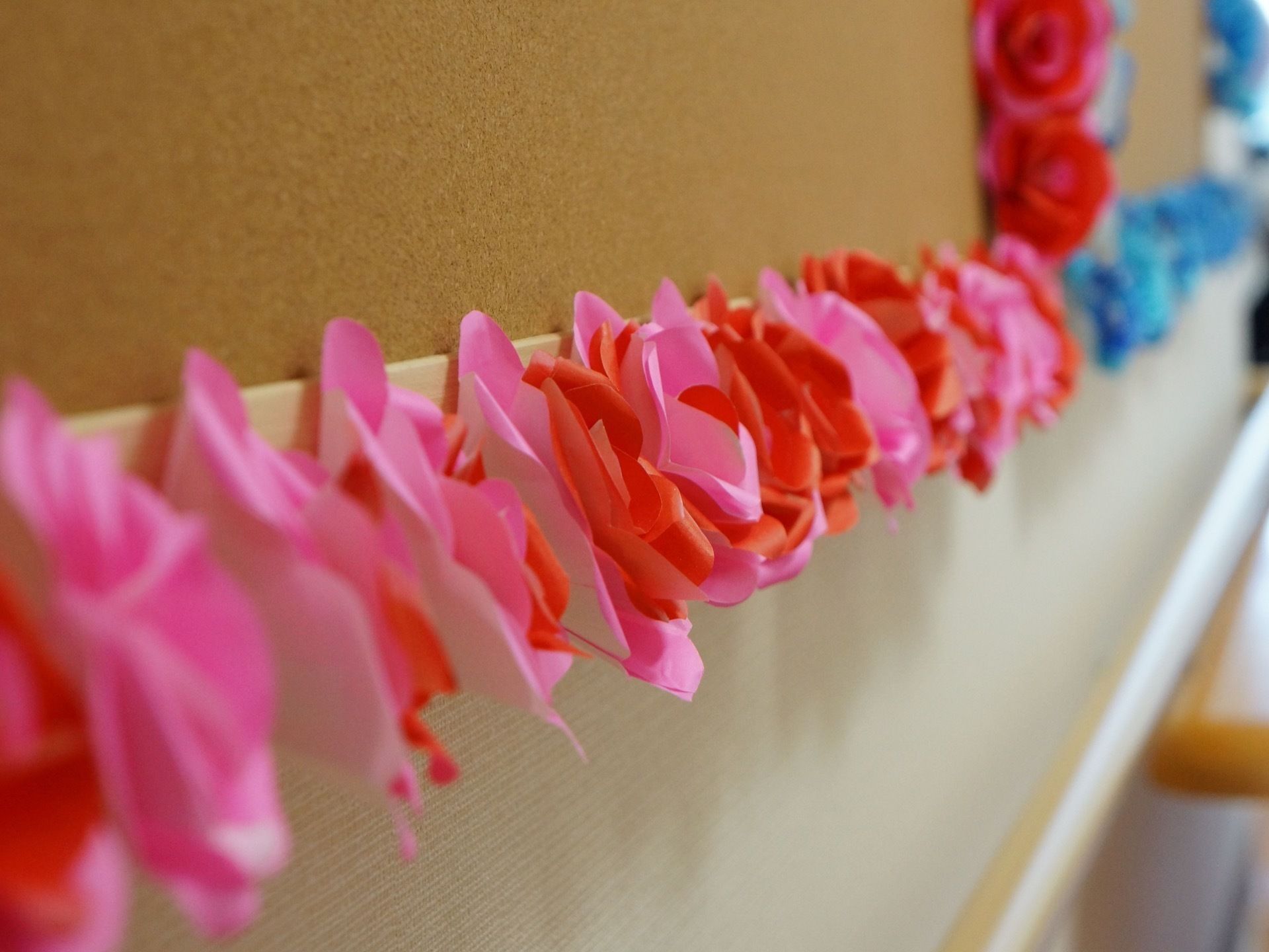 縁の部分に折り紙で作ったピンクや赤色の花が飾られている掲示板