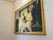 白い壁が広がる場所に絵画が飾られている。絵画は金色の豪華な額に入れられている。2人子どもの天使が肩を寄せ合っている。