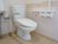 洋式トイレの脇には、跳ね上げ式の肘掛けが備わっている。便器横の壁には手すりとナースコールが設置されている。