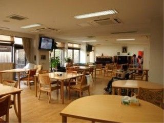 壁一面に大きな窓が設置されている共有スペースである。車椅子をご利用の方がテレビを観ている。室内の奥にピアノが見える。