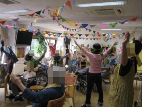 レクリエーションの様子。入居者様が集まって体を動かして楽しんでいる。窓際の壁にはテレビが設置されている。