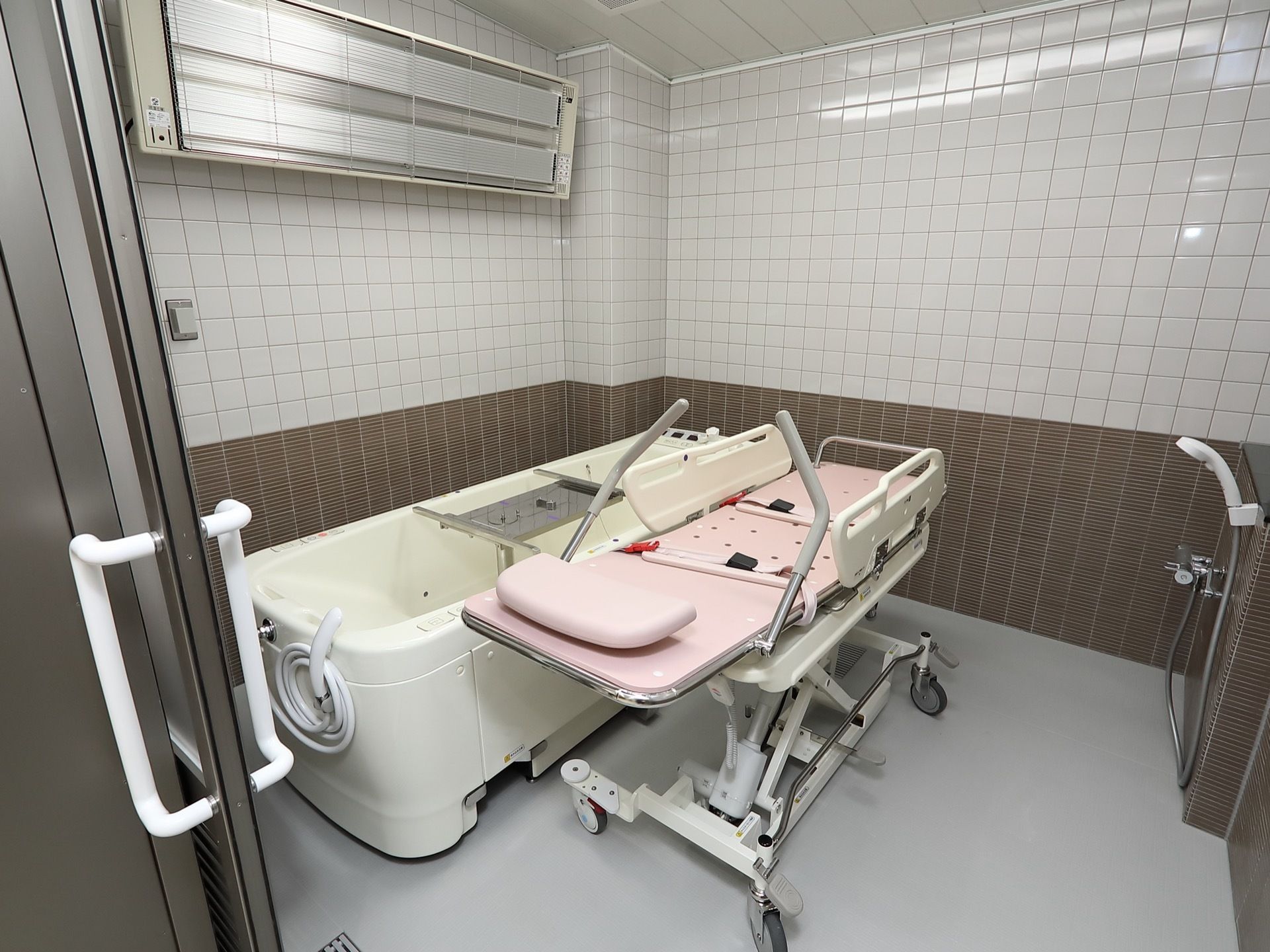 介護浴槽が設置された浴室で、上部に大型のヒーターが取りつけられている。浴室入口はスライド式の扉になっている。