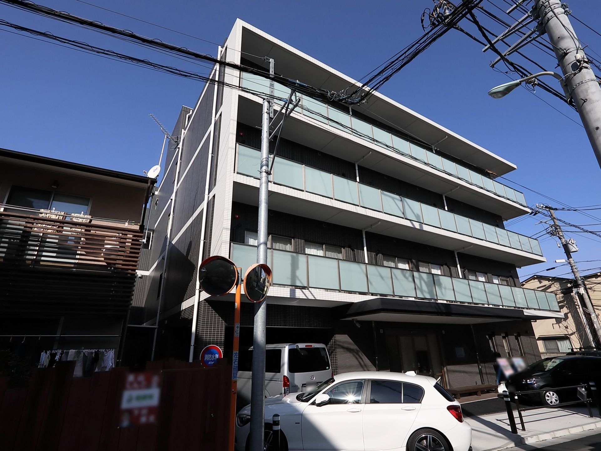 4階建ての建物で、玄関の上部にはひさしが設置されている。施設の両隣には住宅が建てられている。施設前には車が数台停められている。