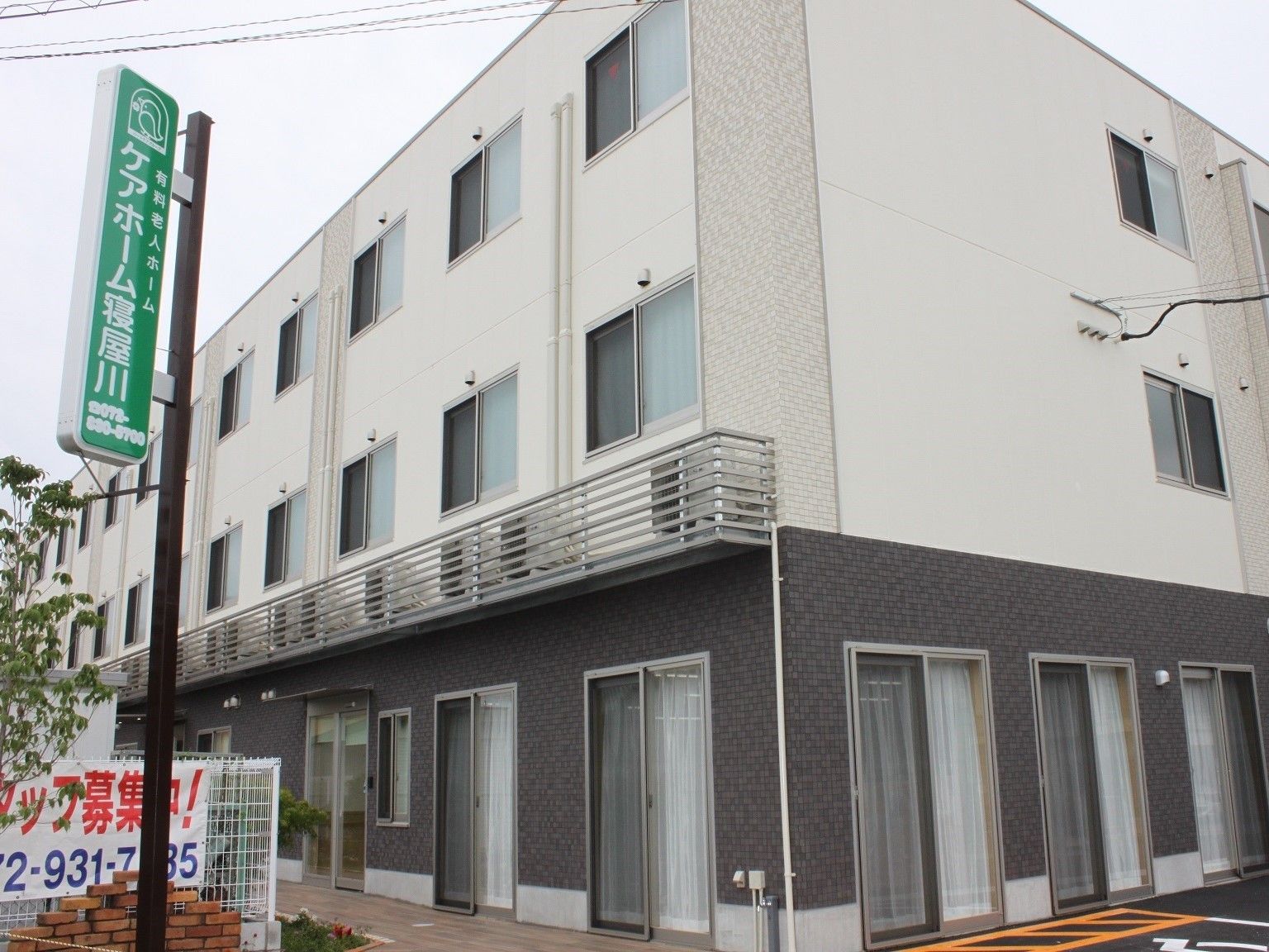 1階部分と2・3階部分で色が分かれている壁。左側には施設名が書かれた看板が立てられている