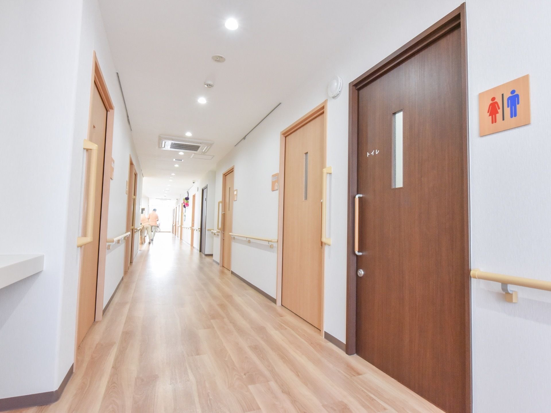 等間隔で照明が取り付けてある明るい廊下。各部屋は開閉しやすいスライド式の扉となっている。手前に共用のトイレが設置されている。