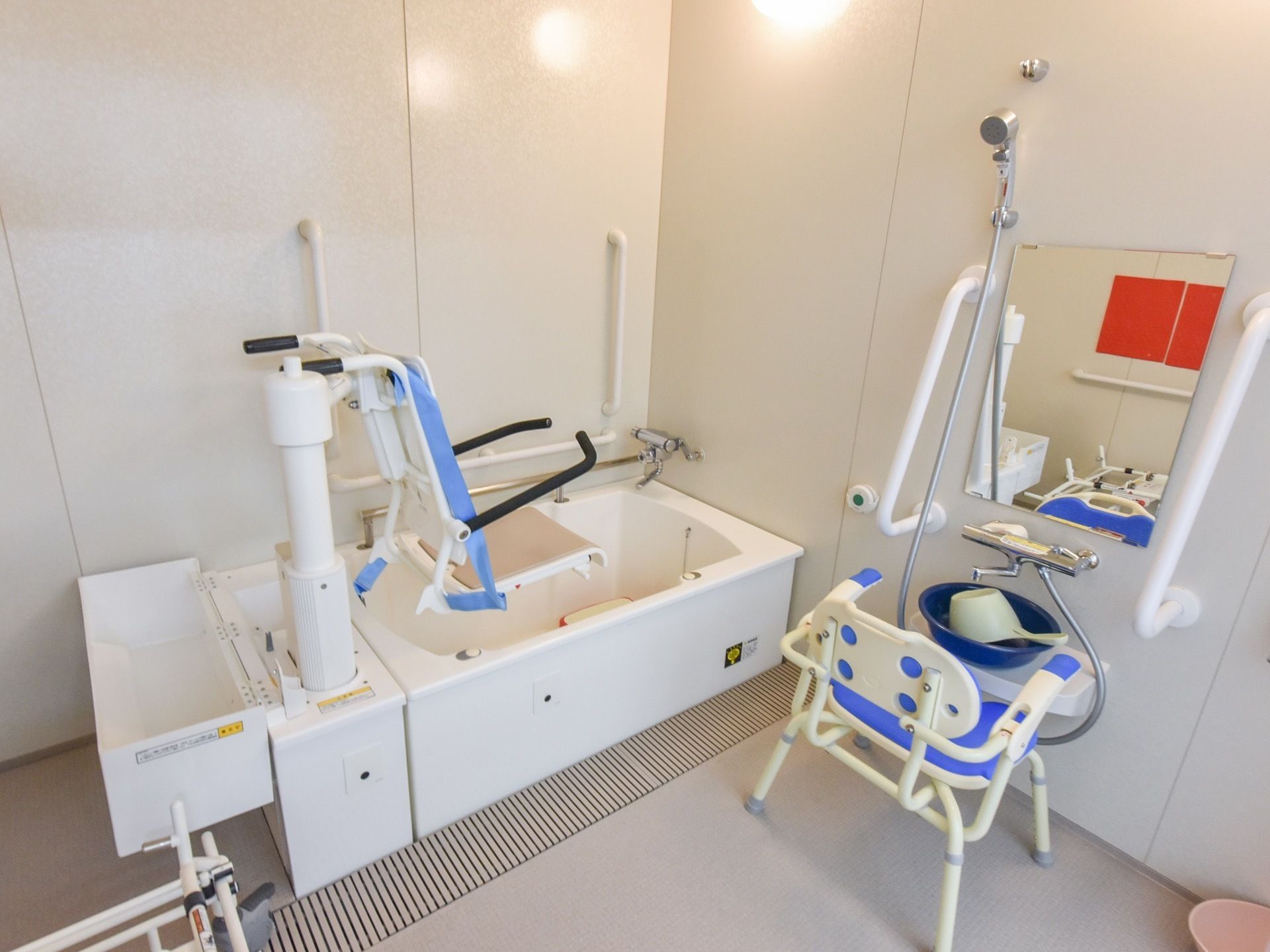 白を基調とした機械浴室。床は滑りにくく、水はけの良い床になっている。鏡が設置された洗い場には、桶が用意されている。