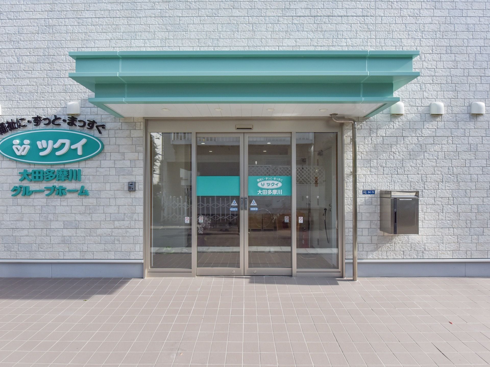緑色の雨よけ屋根がついた自動式の玄関ドアと、扉の横に設置された郵便受け