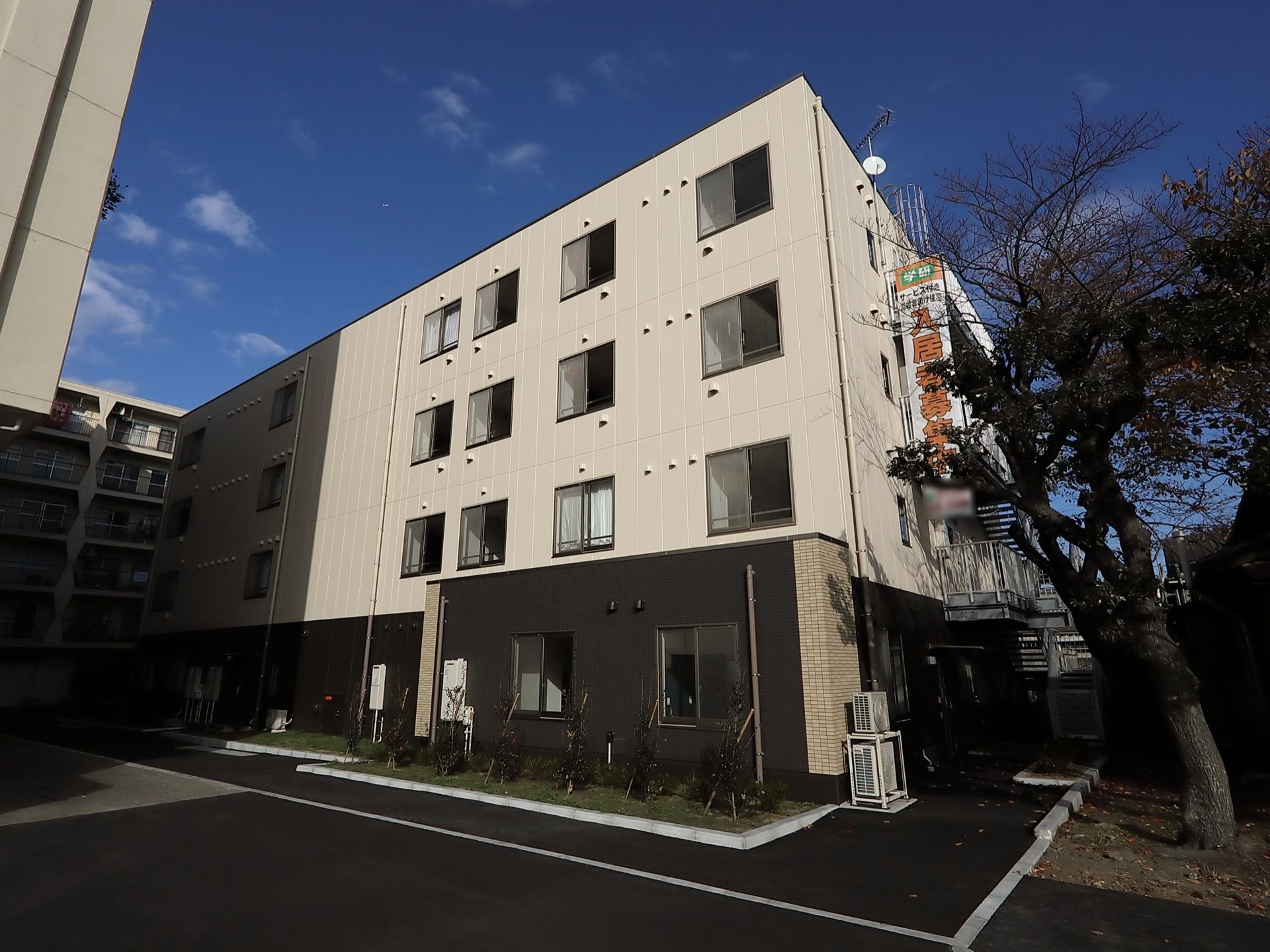 施設の建物周りに多くの木々が植えられている。１階部分にはダークブラウン色の外壁が使われており、モダンな雰囲気である。