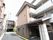 道路に接して建物がある。建物に沿って道路から奥へ続く通路があり、途中に玄関がある。通路には黄色の点字ブロックがある。