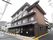 路側帯がカラー舗装されている道路に接して、4階建ての建物が建っている。1階と2階には瓦のひさしがある。