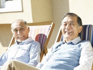 日向ぼっこしながらほほ笑んでいる高齢者男性。リラックスして何かを呼んでいる様子