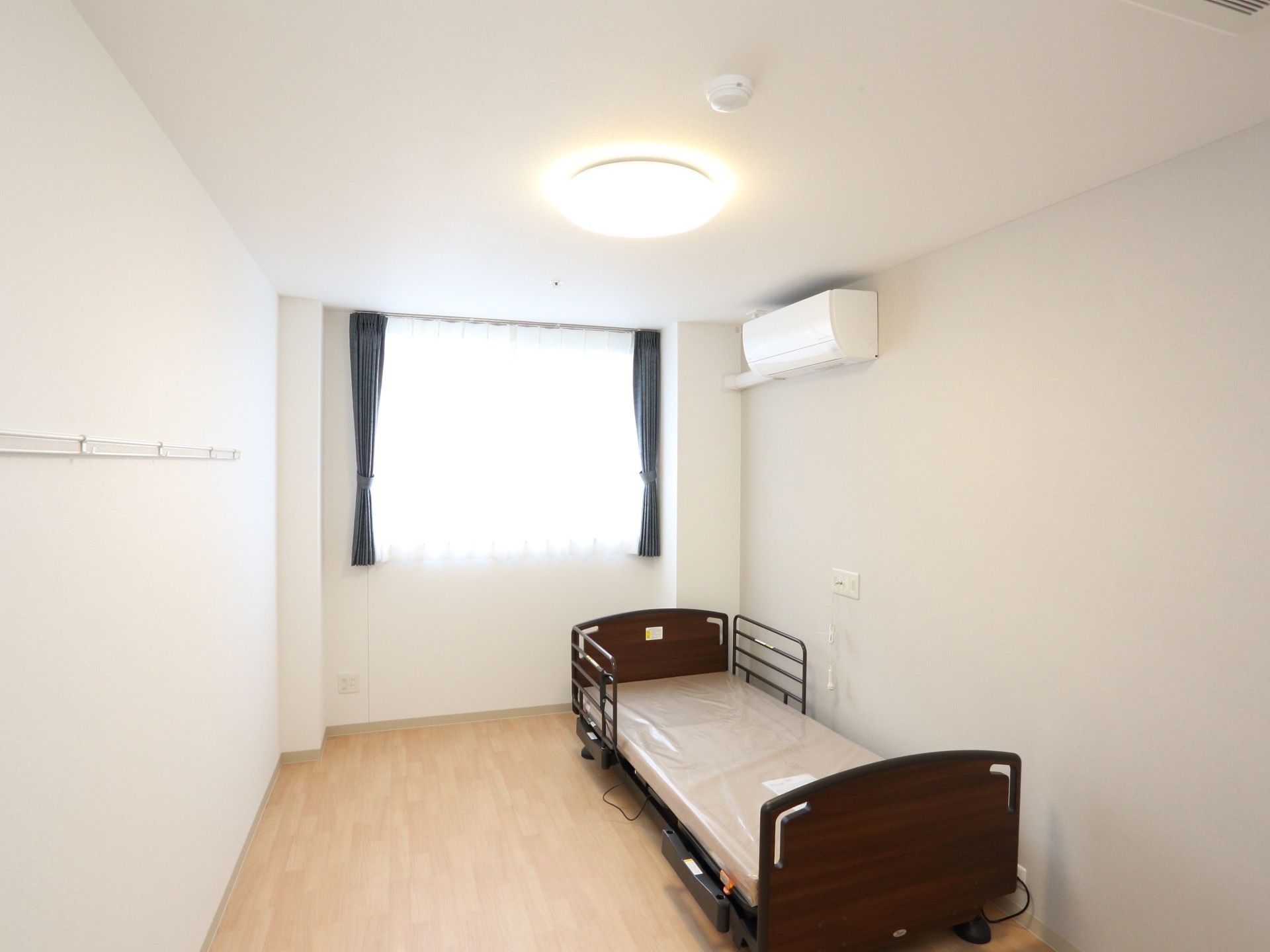 居室の窓からは日が差し込み、部屋全体が明るくなっている。窓にはレースとカラーカーテンがかけられている。ベッド、エアコンが完備されている。