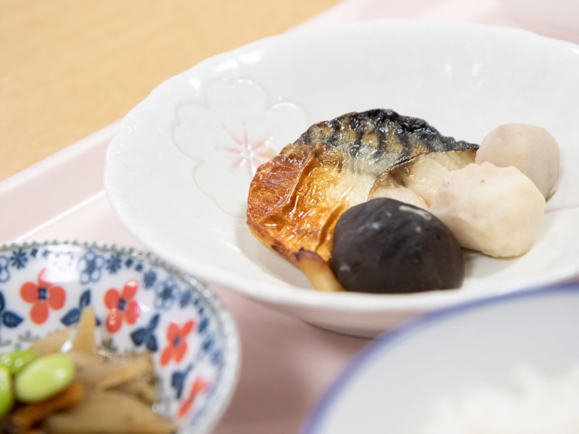 魚と野菜を調理した栄養バランスを考えた、おかずである。それぞれ違う柄のお皿に盛り付けられて、ピンクのトレイに置かれている。