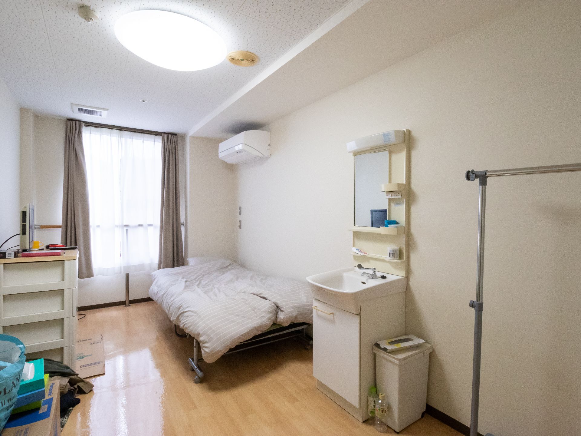 窓辺に手すりがある、ベッドの近くに洗面台が置かれた居室