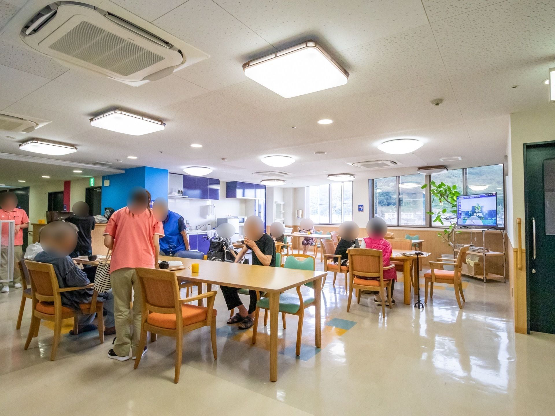青色のキッチンが併設された食堂で食事をする、入居者様と介助をするスタッフ