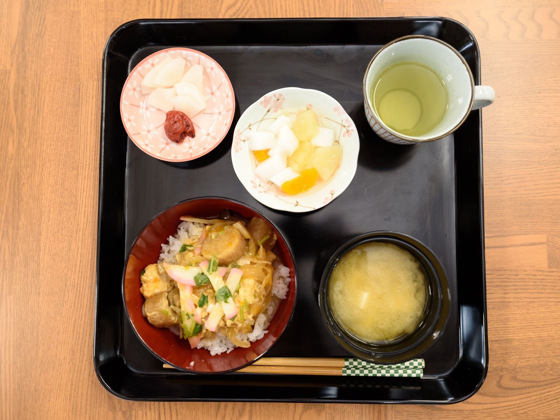 黒色のお盆の上に食事の支度がされている。この日のメニューは丼物と味噌汁、漬物、フルーツ、お茶である。