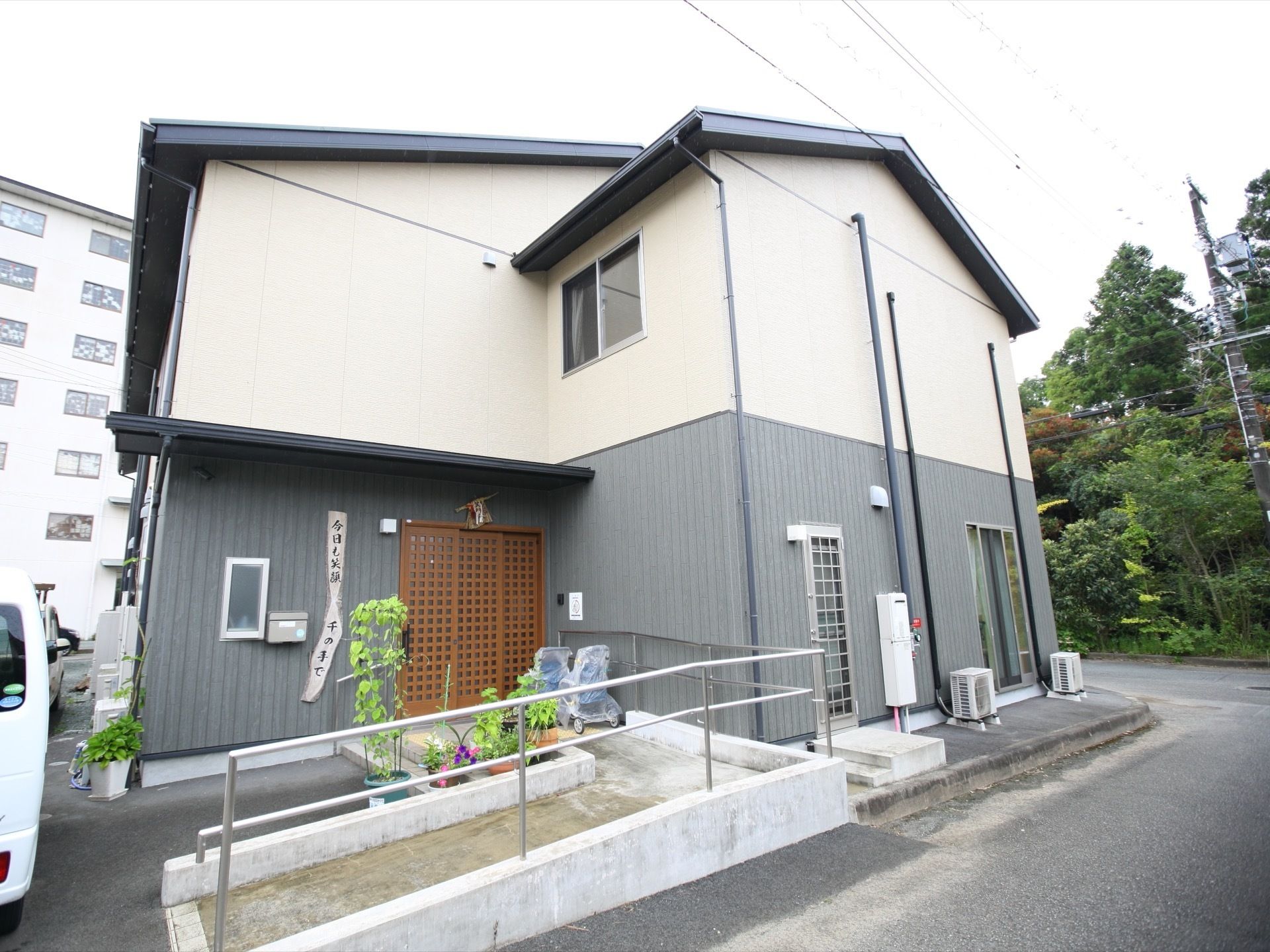 施設は日本家屋風の２階建ての建物である。エントランスには、手すり付きのスロープがある。駐車スペースが建物前に設けられている。