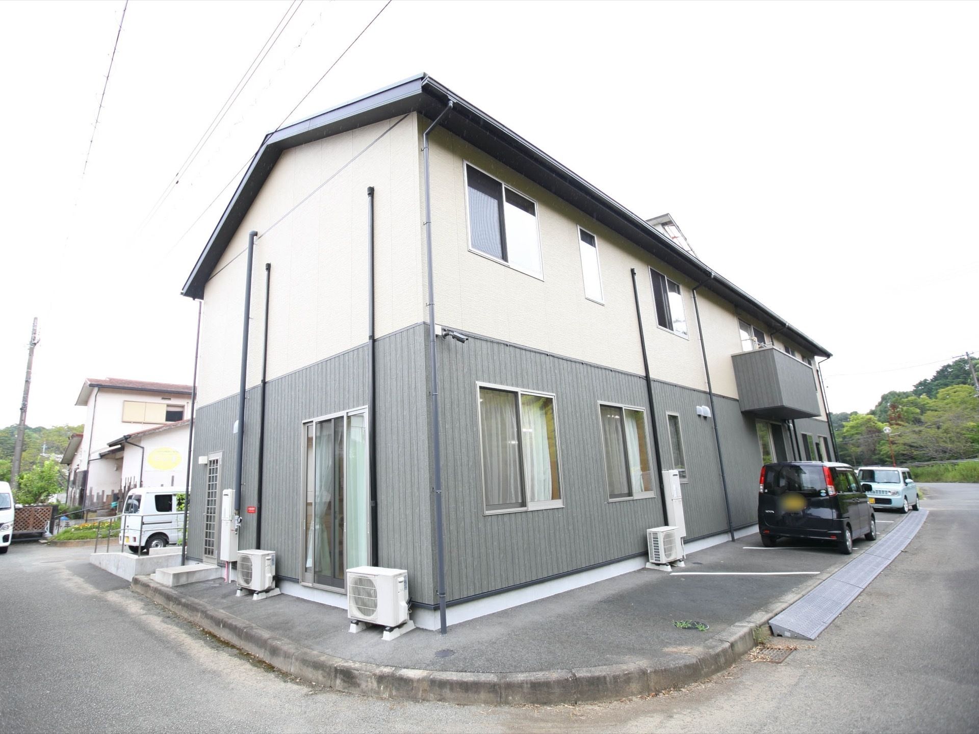 緑に囲まれた立地に建っている２階建ての施設である。手すりを備えたスロープがエントランスに設けられている。