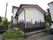 一般住宅を利用したデイサービスセンターの建物である。手すり付きの階段が設けられている。外壁に施設名が書かれた看板がある。