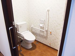 手すりを張り巡らしたトイレは、足元が不安な入居者様も安心な造りである。白い便器は清潔感を感じさせる。