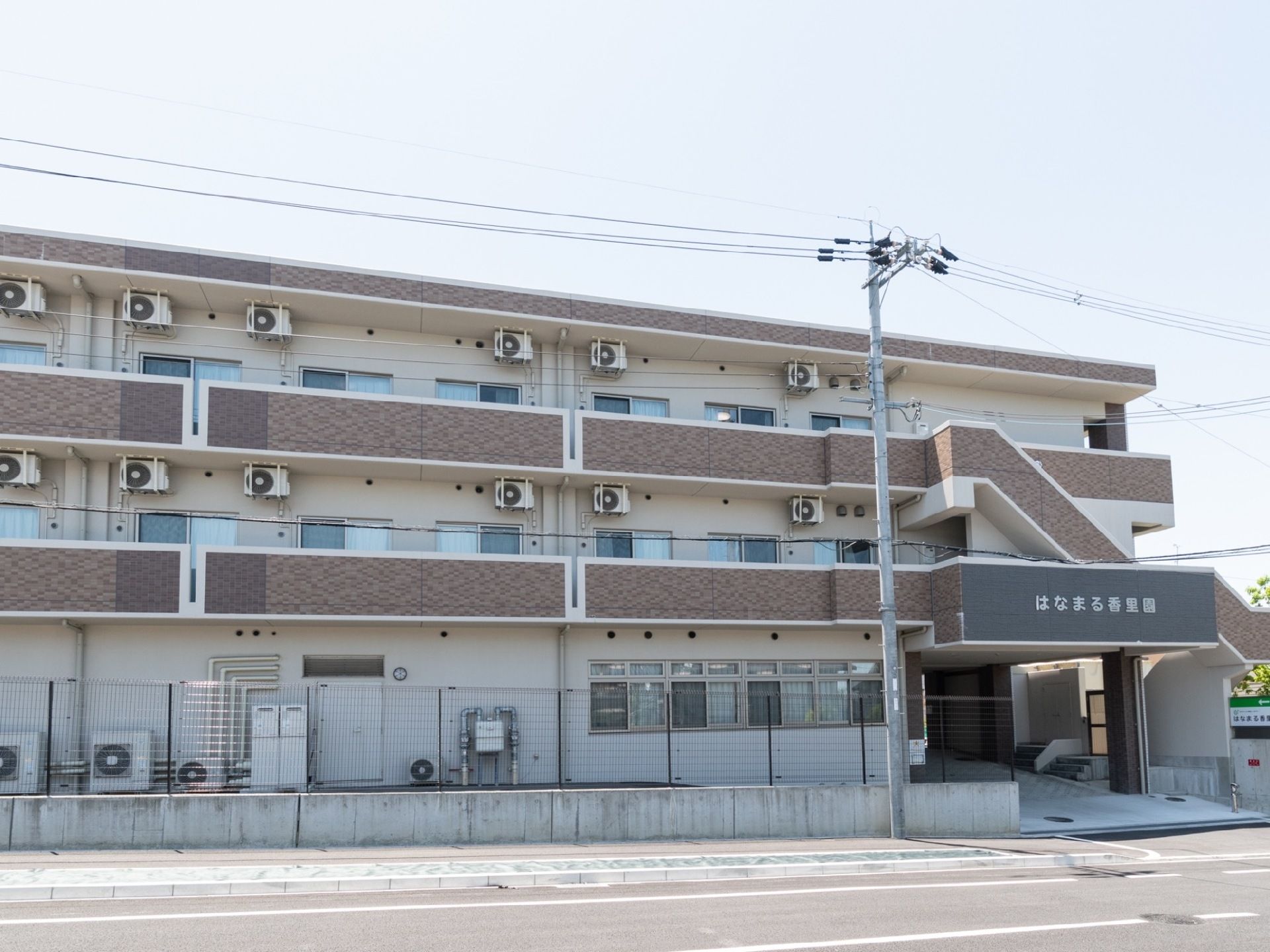 3階建ての建物で、駐車スペースへ向かうには建物をくぐる形になっている。各部屋のベランダに室外機が設置されている。