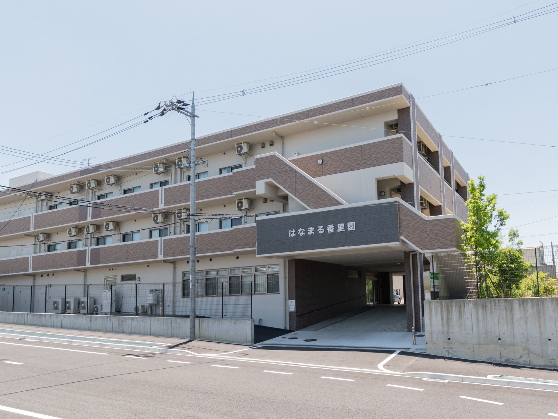 ３階建てのレンガとクリーム色のビルのような建物である。施設名が書かれた１階部分に、駐車場へ続くスロープが設置されている。