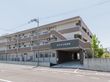 ３階建てのレンガとクリーム色のビルのような建物である。施設名が書かれた１階部分に、駐車場へ続くスロープが設置されている。